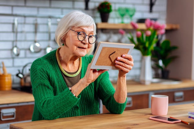 woman in emerald cardigan and stylish glasses cheerfully admiring photo