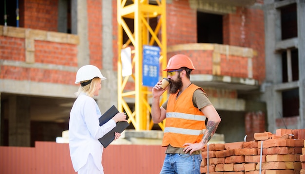 Woman engineer and brutal builder communicate construction site\
background construction team communication concept relationships\
between construction clients and participants building\
industry