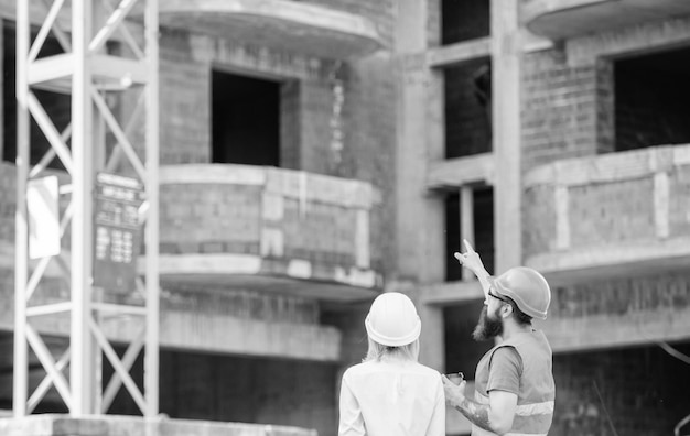 Woman engineer and builder communicate at construction site Relationships between construction clients and participants building industry Construction team communication concept Discussing plan