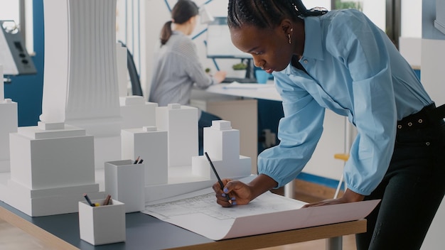 建設レイアウトを設計するためにテーブルの青写真計画を見ている女性エンジニア。建築モデルを分析し、近代建築プロジェクトを計画する専門の建築家。都市開発