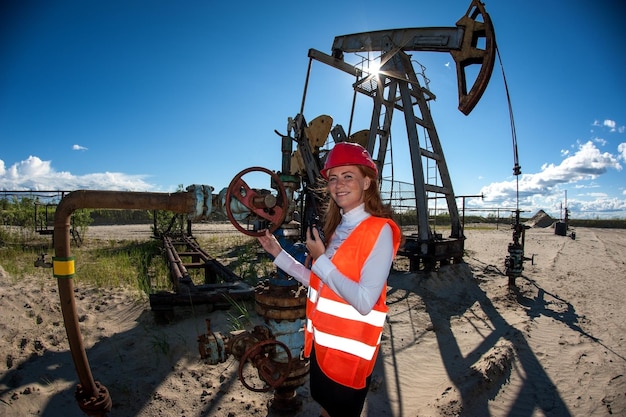 Photo woman engineer in the oil field talking on the radio wearing red helmet and orange work clothes. industrial site background.