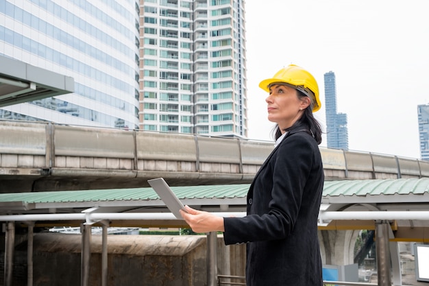 L'ingegnere della donna con il casco sta tenendo il computer portatile sullo sky train in urbano