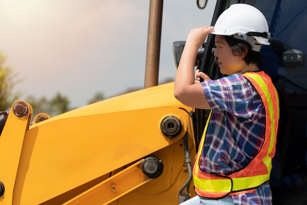 Woman Engineering wearing a white safety helmet standing In front of the backhoe