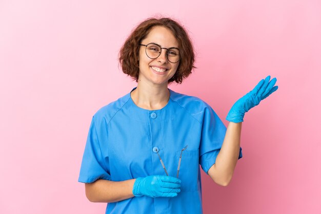 Woman English dentist holding tools over isolated on pink background extending hands to the side for inviting to come