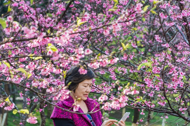 桜の木の下で公園でセルフをした後、スマートフォンで写真を楽しむ女性