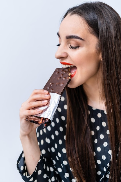 Woman enjoying a chocolate bar with enthusiasm indoors A young woman bites into a chocolate bar