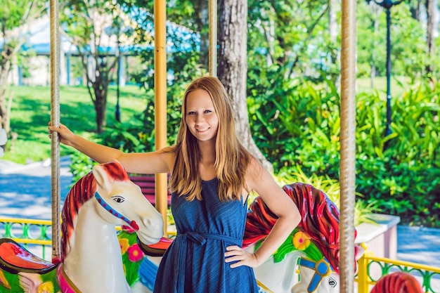 Woman enjoying in funfair and riding on colorful carousel house.