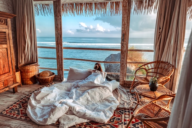 Женщина, наслаждаясь утренние каникулы на бунгало на тропическом пляже, глядя на океан Расслабляющий отдых на Улувату Бали, Индонезия