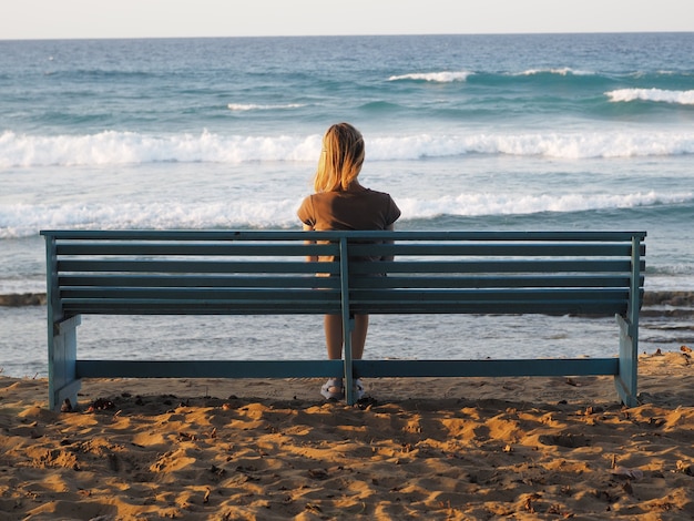 写真 日没のベンチから海の景色を楽しむ女性。背面図。