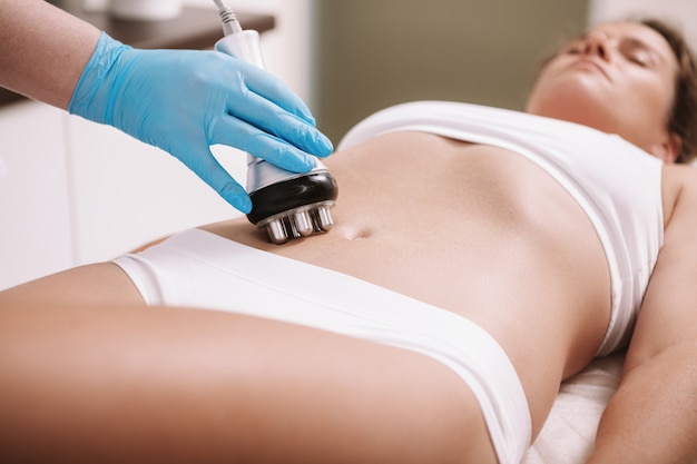 Woman enjoying rf-lifting procedure on her stomach skin at beauty clinic