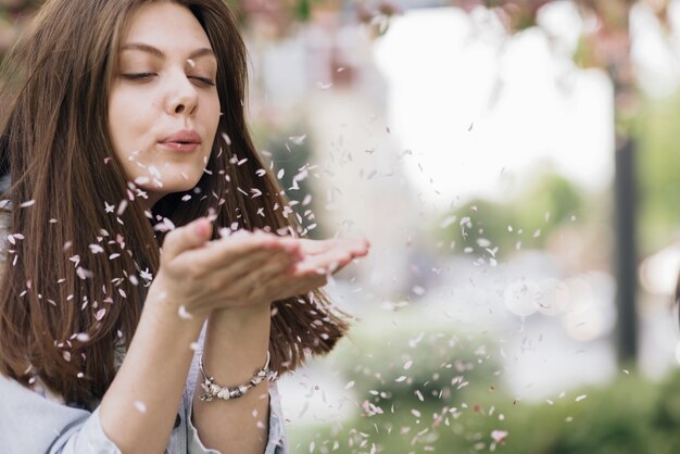 Foto donna che si gode la fioritura primaverile ragazza felice che soffia petali di fiori di sakura facendoli volare