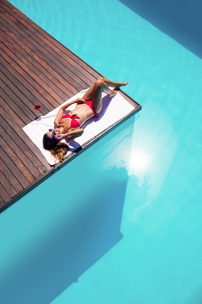 Женщина, наслаждаясь солнечными ваннами на краю бассейна