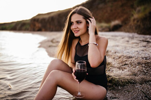 A woman enjoys a glass of wine overlooking the mediterranean sea during an intense summer sunset in Greece