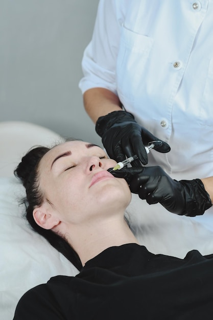 한 여성 이 미용사 의 히알루론산 으로 입술 을 확대 한다. 주사 미용학 입술 필러