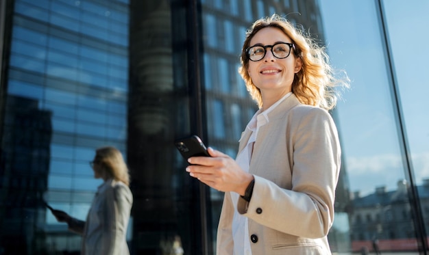 여성 기업가가 전화를 사용하여 고객의 이메일에 답장하고 있습니다. 얼굴에 안경을 쓰고 출근합니다.