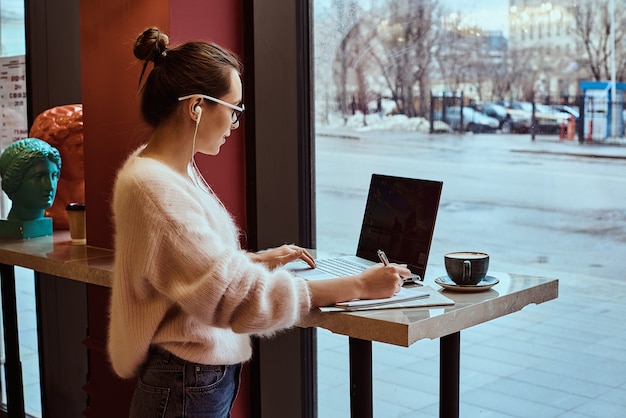 Woman entrepreneur working from cafe and talking on mobile phone with headphones