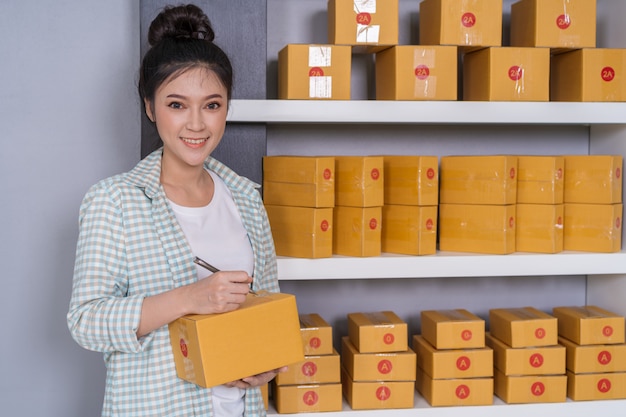 Woman entrepreneur writing on parcel box, online business, prepare before delivery