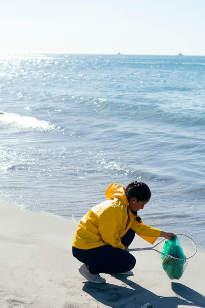 Woman environmentalist picking up a bag of garbage while crouching on the beach