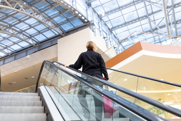 Woman on escalator staircase in business centrerear view of woman while using escalator in shopping mall