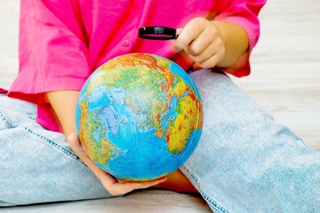 Photo a woman examines the globe she holds in her hands with a magnifying glass