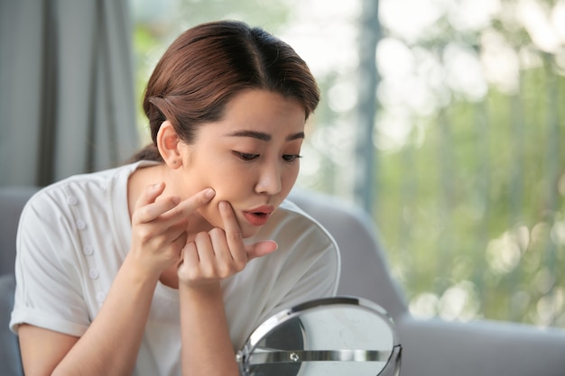 Woman examining her face in the mirror, problematic acne-prone skin concept