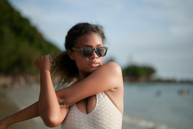 La donna esercita e allunga i muscoli prima dell'allenamento all'aperto ritratto sexy signora africana asiatica che si prepara per il fitness in spiaggia