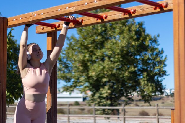 Woman exercising while hanging from one bar to another in an outdoor gym, horizontal view