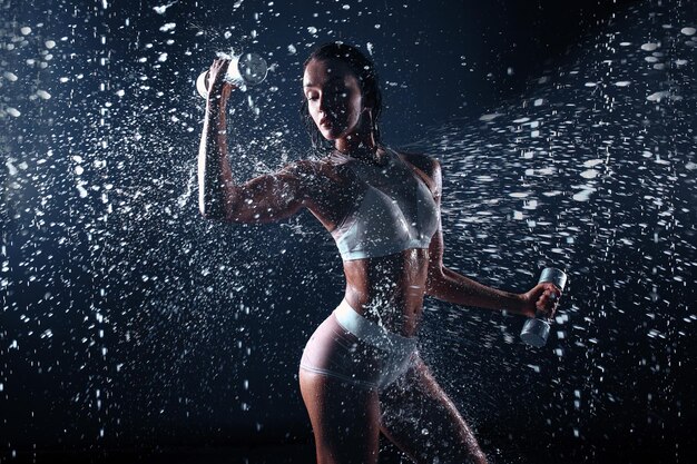Woman exercising with dumbbell in water against black background