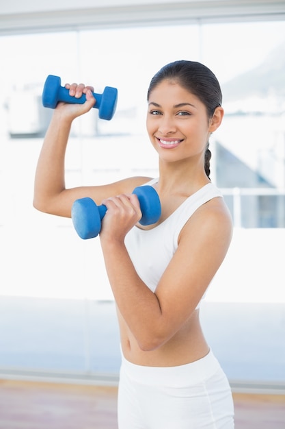 Donna che si esercita con i dumbbells nello studio di forma fisica