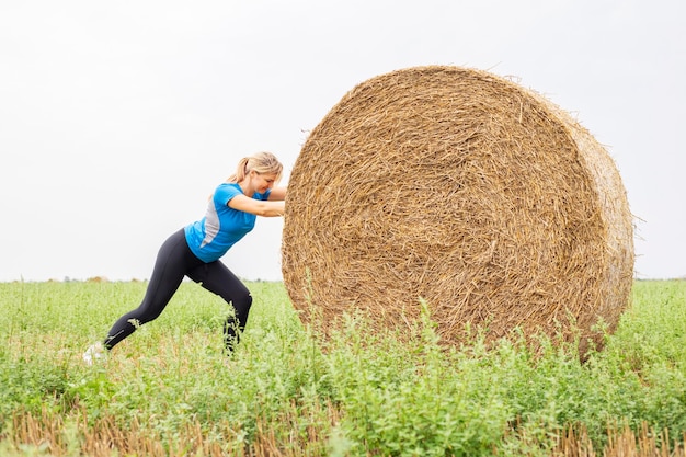 Woman exercising with hay bale in field