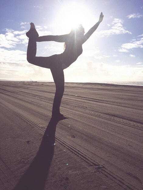 Foto donna che fa yoga sulla sabbia sulla spiaggia contro il cielo