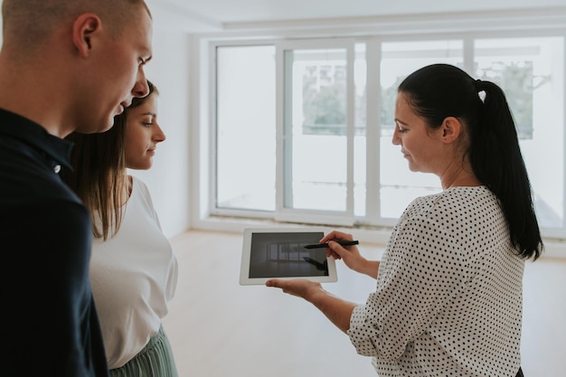 Photo woman explaining blueprint to couple on tablet at home