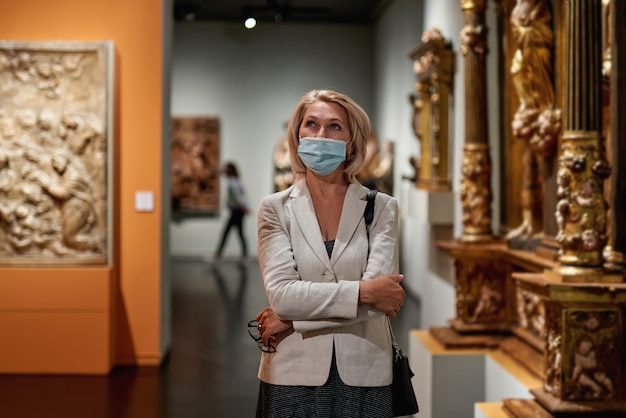 Woman exploring medieval expositions in museum wearing an antivirus mask