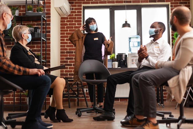 Woman expressing anger management issues at aa meeting, wearing face mask. People attending group therapy session for support and guidance against addiction and depression during pandemic.