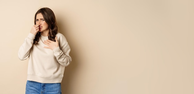 Woman expressing disgust of bad disgusting smell close nose and grimaing from dislike standing over