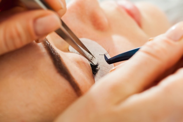 Photo woman eye close up during the eyelash extension procedure. macro, selective focus.