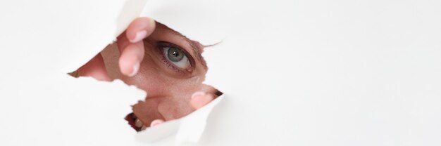 Woman eye looks through hole in white paper