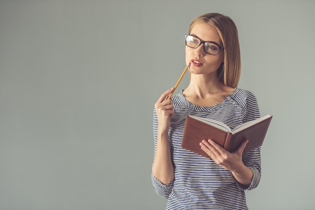 Woman in eyeglasses is holding a pencil and a notebook