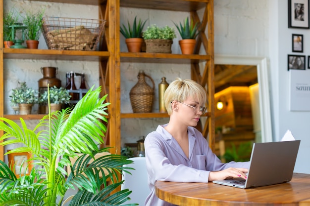 Woman in eyeglasses works with documents in front of a laptop monitor in home interior