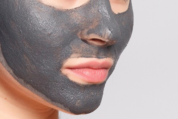 Photo woman face mask portrait of beautiful girl removing cosmetic black peeling mask from facial skin closeup of attractive young woman with natural makeup and cosmetic peel mask on face high resolution