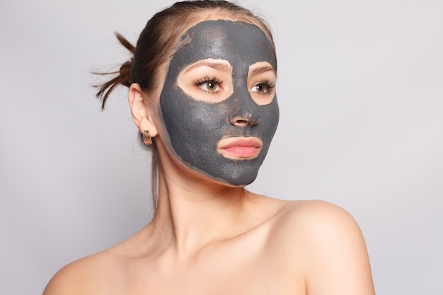 Maschera per il viso della donna. ritratto di una bella ragazza che rimuove la maschera peeling nera cosmetica dalla pelle del viso. primo piano di giovane donna attraente con trucco naturale e maschera di buccia cosmetica sul viso. alta risoluzione