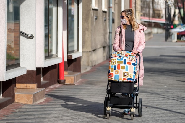 Foto donna in maschera che spinge un passeggino in città