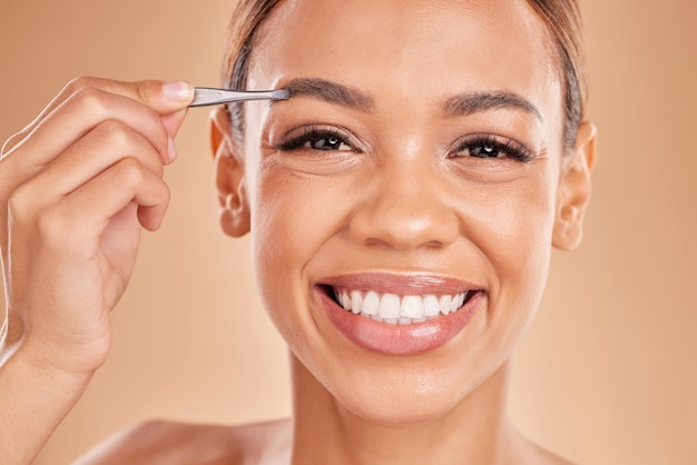 Woman face and tweezer on eyebrow for skincare beauty grooming or trimming against a studio background portrait of happy female tweezing eyebrows with big smile for facial cleaning or hair removal