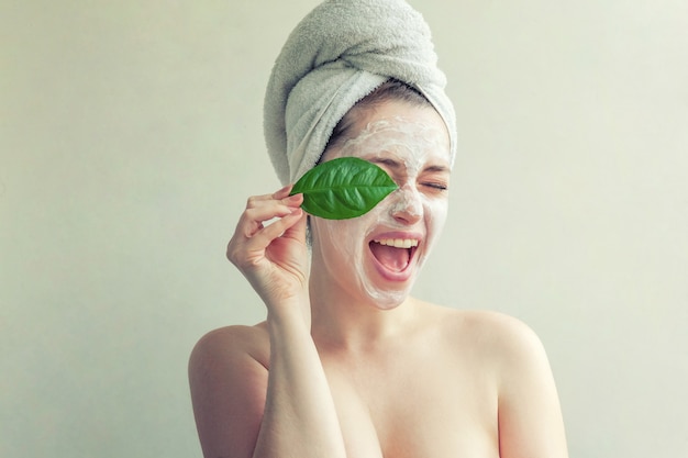 緑の葉とクリームまたは栄養マスクを持つ女性の顔