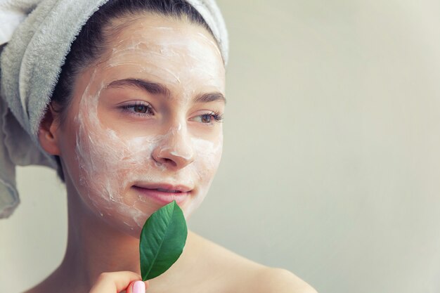 Woman face with green leaf and cream or nourishing mask