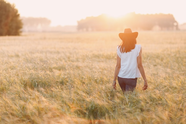 Contadina in cappello da cowboy che cammina al campo agricolo sul tramonto.