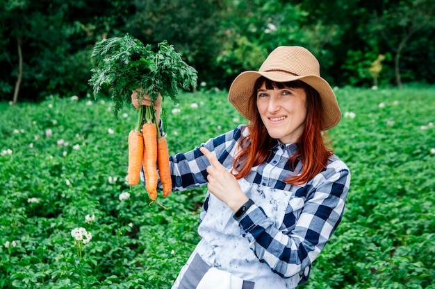 Woman farmer holds a bunch of carrots on background vegetable garden