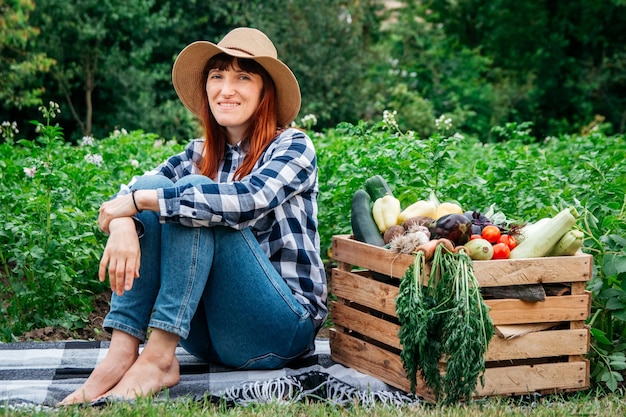 Woman farmer sitting near fresh organic vegetables in a wooden box on background vegetable garden