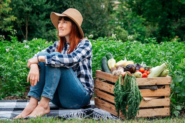 Woman farmer sitting near fresh organic vegetables in a wooden box on background vegetable garden