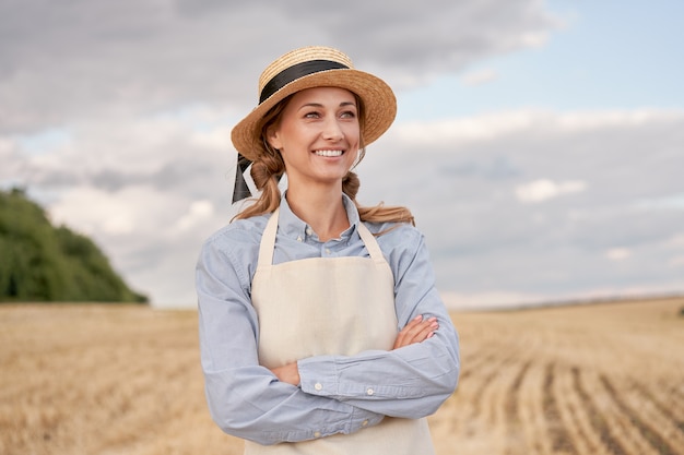 Woman farmer straw hat apron standing farmland smiling Female agronomist specialist farming agribusiness Happy positive caucasian worker agricultural field